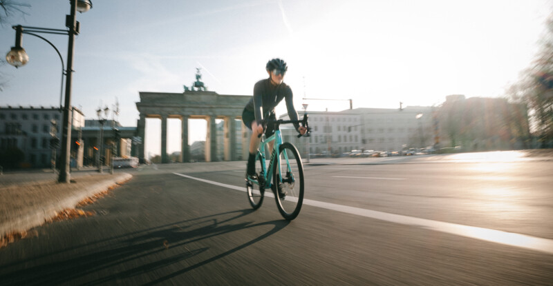 Ein Radfahrer fährt dynamisch auf leerer Straße am Brandenburger Tor entlang, im Morgenlicht.