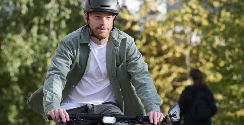 A man wearing a helmet rides a bicycle through green surroundings while looking ahead.